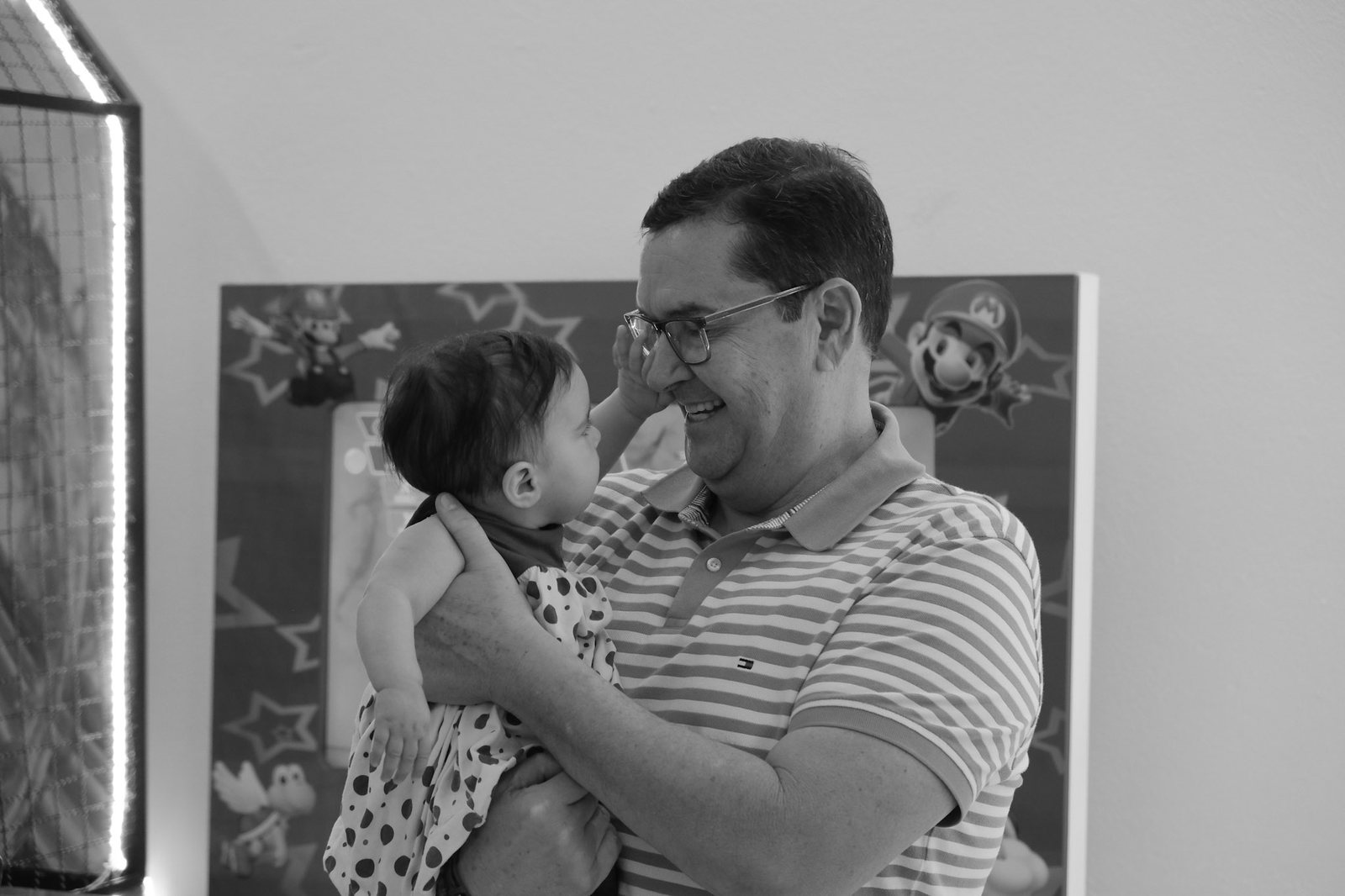 Homem de óculos segurando um bebê no colo e sorrindo, em preto e branco