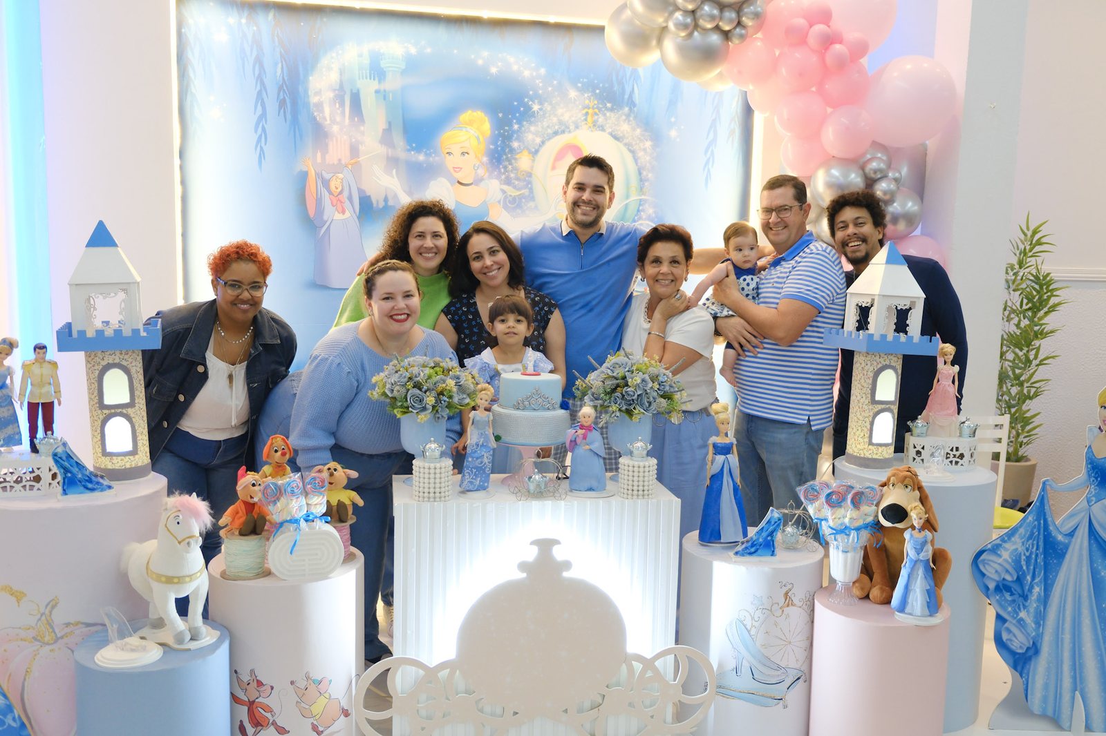 Família e convidados reunidos atrás da mesa decorada de uma festa com tema de Cinderela
