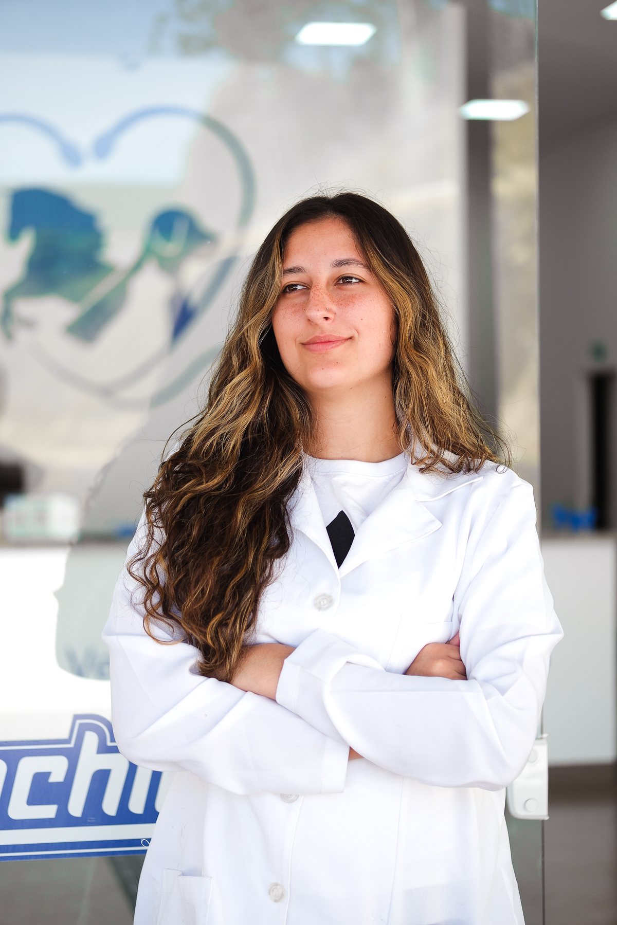 Moça de jaleco branco e braços cruzados, num retrato de equipe dentro da clínica