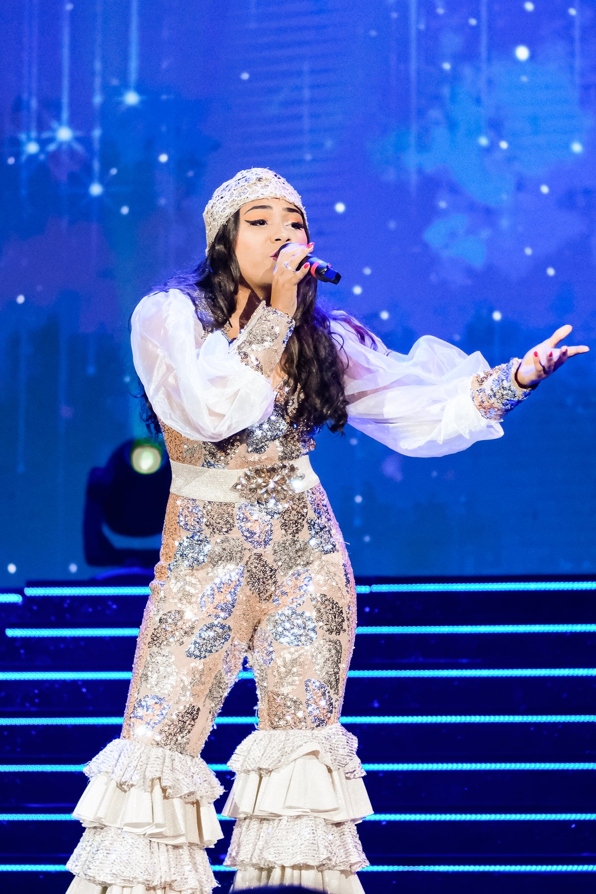 Cantora de turbante e roupa brilhante abrindo o braço no palco